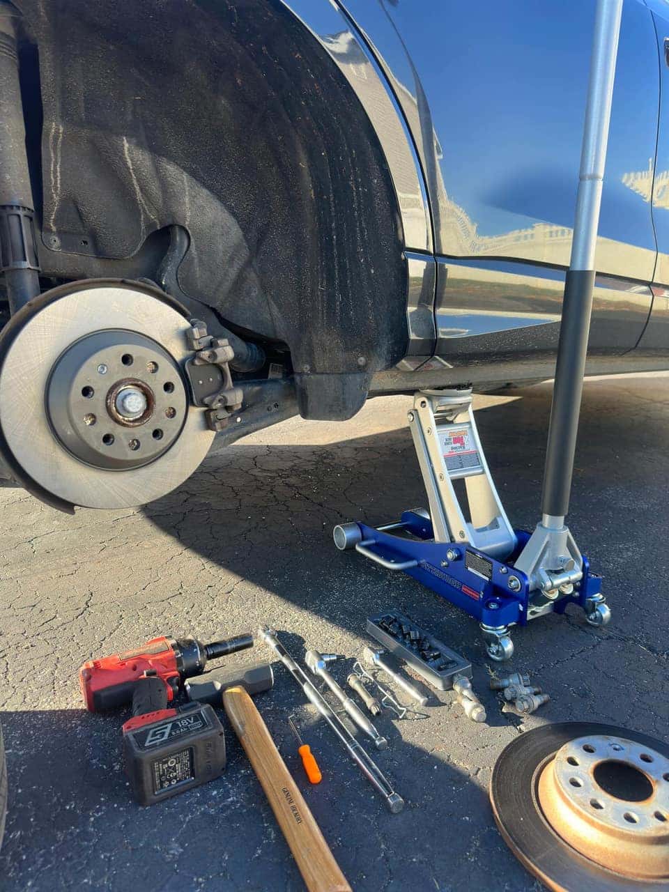 Front brake job underway: old rotor off, new rotor and impact wrench laid out by a jacked-up car