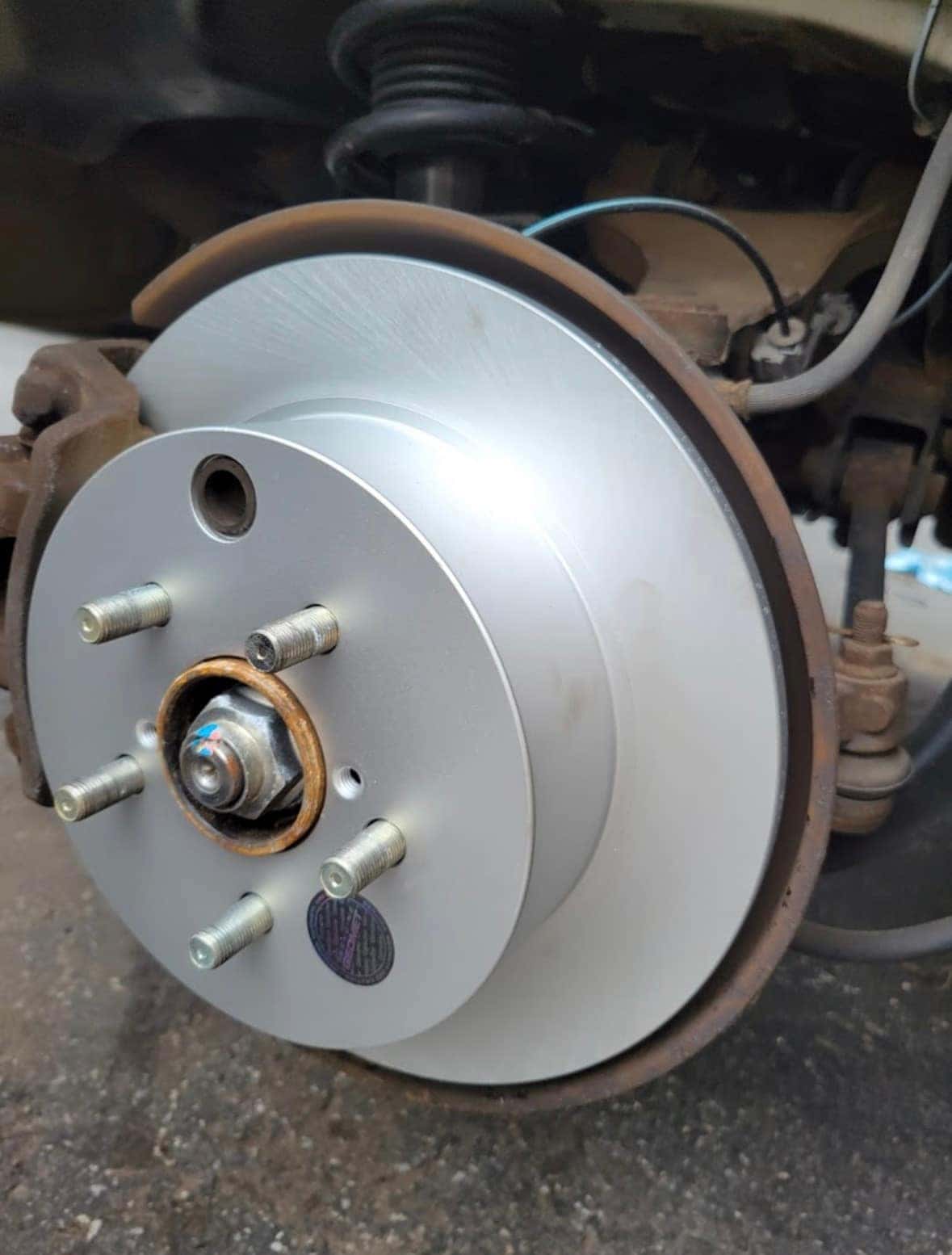 Close-up of a freshly installed front brake rotor and clean wheel hub with new studs