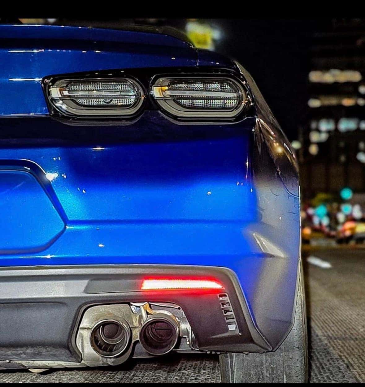 Rear of a blue Chevrolet Camaro SS at night showing dual exhaust tips and an LED tail-light bar