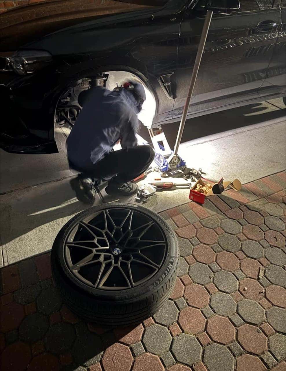 Night-time mobile brake and wheel service on a black BMW, forged wheel off on the ground