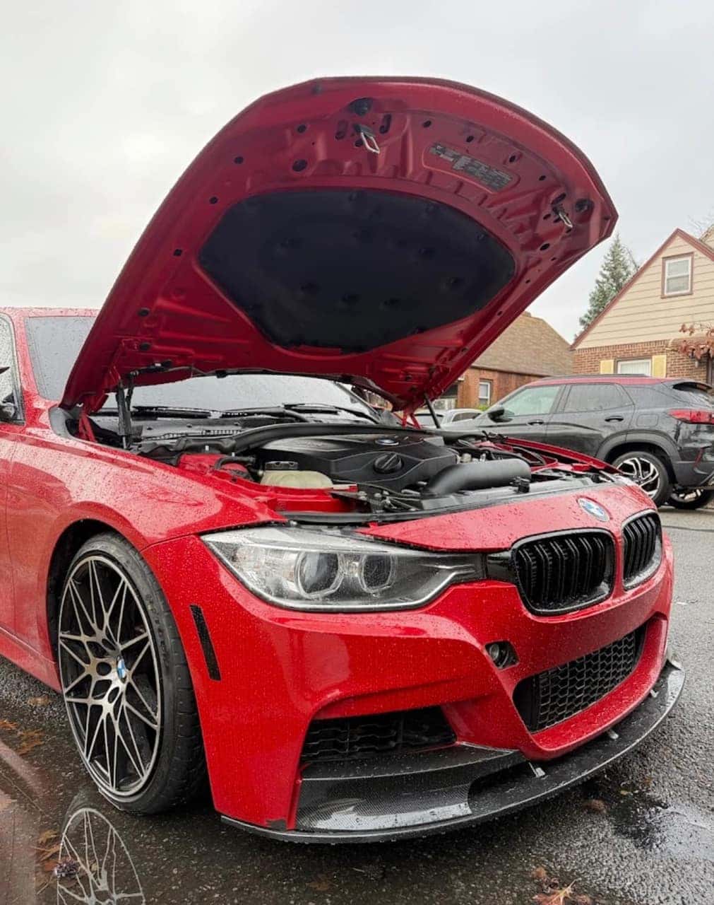Red BMW 3 Series with the hood up for service in a driveway, M-style wheels and a carbon front lip