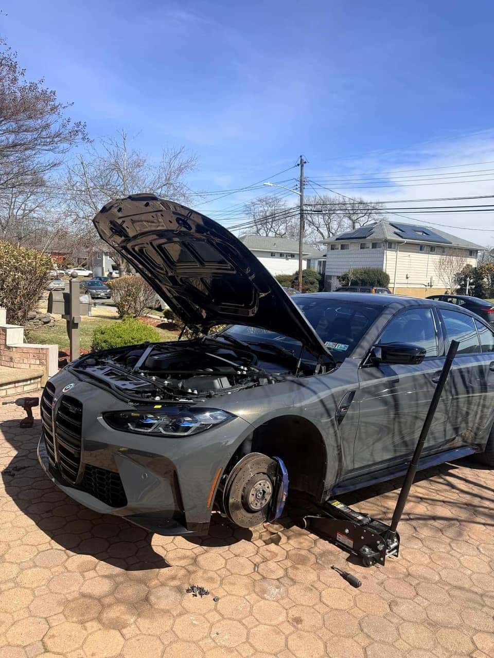 Grey BMW M4 up on jack stands with a front wheel removed during a driveway service call
